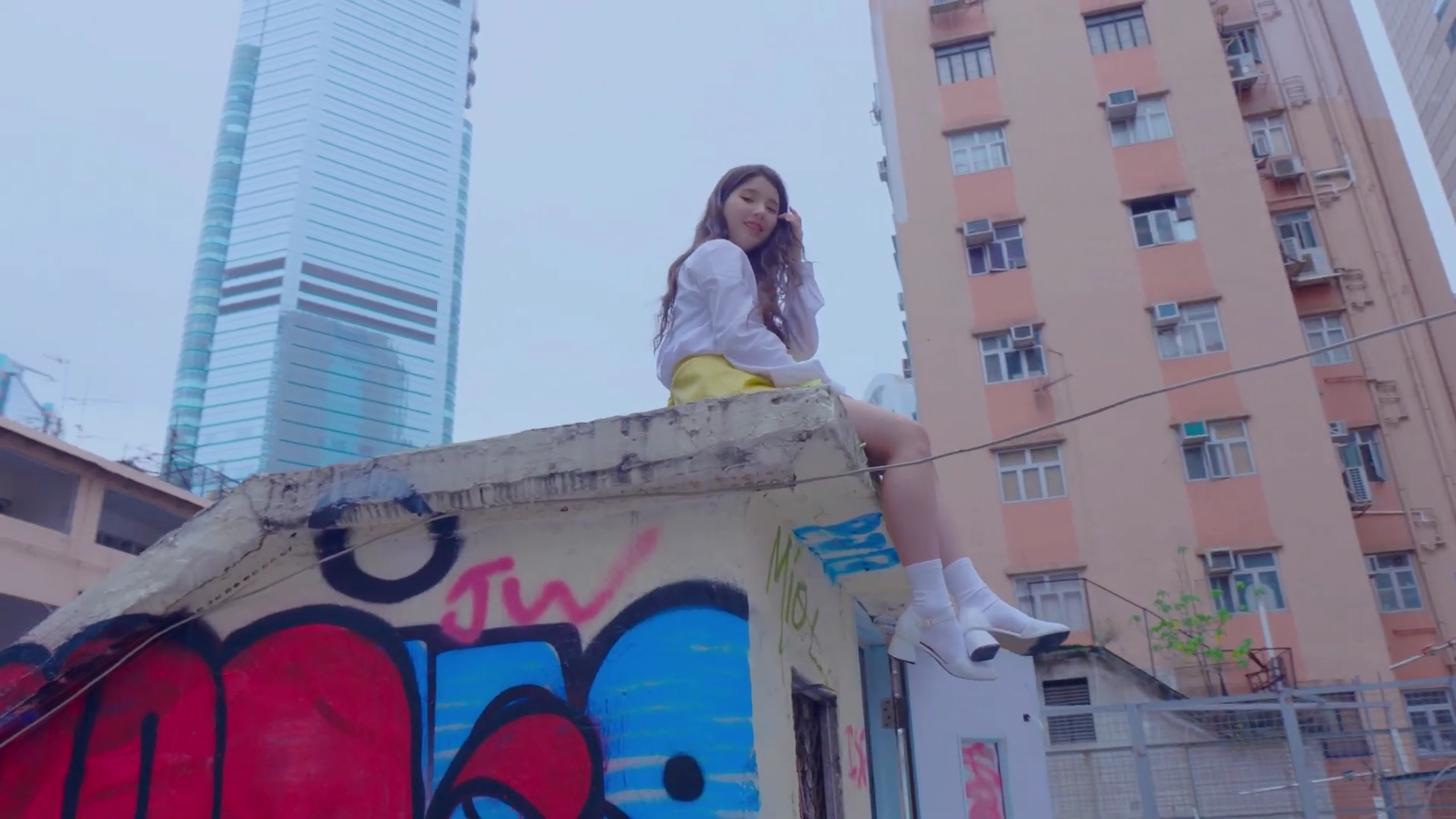 Heejin sitting on top of a structure covered in graffiti.